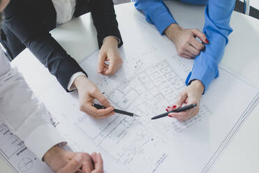 Close-up of businessman and two businesswomen working on plan on desk in office - MOEF02600