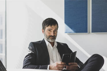 Porträt eines selbstbewussten reifen Geschäftsmannes mit Mobiltelefon im Büro - MOEF02612