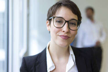 Portait of confident young businesswoman with man in background - MOEF02620