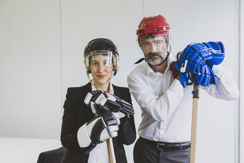 Porträt einer Geschäftsfrau und eines Geschäftsmanns mit Eishockeyausrüstung im Büro - MOEF02635