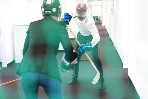 Geschäftsfrau und Geschäftsmann spielen Eishockey im Büro, lizenzfreies Stockfoto