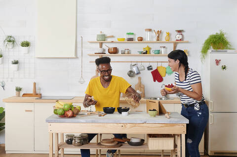 Lachendes multiethnisches Paar, das gemeinsam in der Küche frühstückt, lizenzfreies Stockfoto