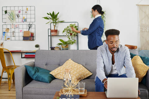 Multiethnisches Paar verbringt Zeit zusammen im Wohnzimmer, Mann benutzt Laptop, lizenzfreies Stockfoto