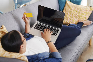 Junge Frau benutzt einen Laptop und liegt auf einem Sofa - IGGF01431