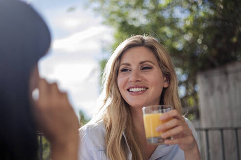 Zwei Frauen frühstücken an einem Cafétisch im Freien, haben Spaß und unterhalten sich - AJOF00036