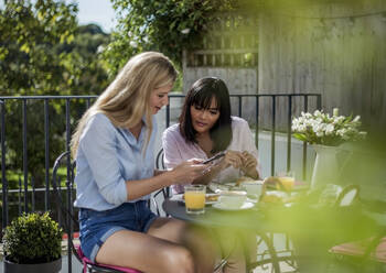 Zwei Frauen, die ihr Smartphone überprüfen, frühstücken in einem Straßencafé - AJOF00039