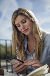 Frau schreibt in der Nähe eine SMS auf ihrem Smartphone, im Freien - AJOF00041