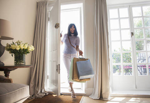 Frau mit Einkaufstüten, die durch die Eingangstür kommt, lizenzfreies Stockfoto