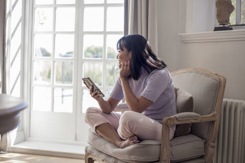 Woamn sitzt auf einem Sessel und benutzt ein Smartphone - AJOF00051