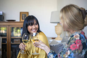 Two friends sittng on couch, drinking wine, smiling - AJOF00059