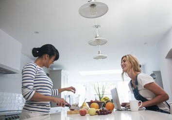 Two friends preparing fresh smoothie, chopping fruits in the kitchen - AJOF00066