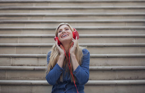Porträt einer lächelnden Frau, die mit roten Kopfhörern Musik hört - AJOF00072