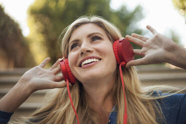 Porträt einer lächelnden Frau, die mit roten Kopfhörern Musik hört - AJOF00073
