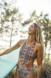 Junge blonde Frau mit einem Surfbrett im Wald - MTBF00091