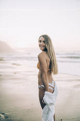 Young blond woman wearing bikini at the beach during sunrise - MTBF00112