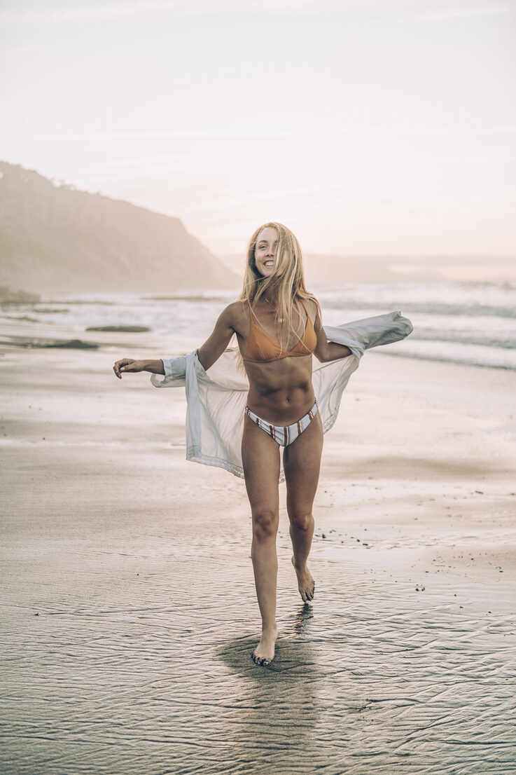 Young blond woman wearing bikini at the beach during sunrise stock photo