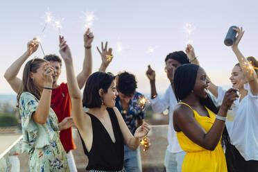 Group of happy multi-ethnic friends celebrating a party in the evening, holding sparklers - SODF00185