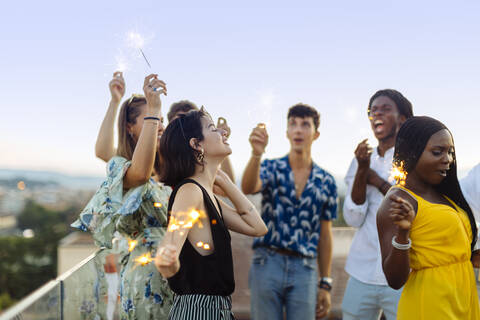 Gruppe fröhlicher multiethnischer Freunde, die abends eine Party feiern, mit Wunderkerzen in der Hand, lizenzfreies Stockfoto