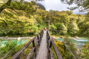 Wanderin, die über eine Drehbrücke über einen Fluss läuft, Fiordland National Park, Südinsel, Neuseeland - SMAF01662