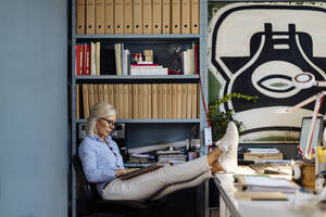 Reife Frau bei der Arbeit im Architekturbüro, die Füße hochgelegt - SODF00212