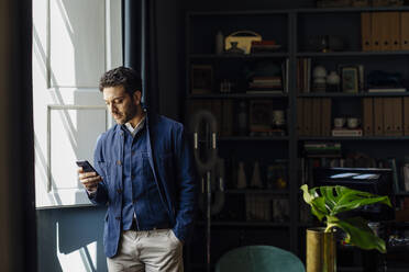 Mann steht in seinem Büro und benutzt sein Smartphone - SODF00234