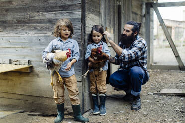 Vater mit zwei Kindern im Hühnerstall auf einem Biohof - SODF00307