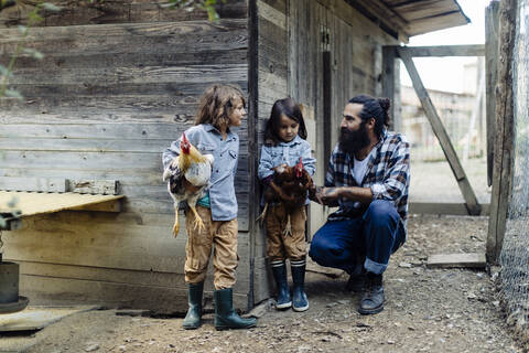 Vater mit zwei Kindern im Hühnerstall auf einem Biohof, lizenzfreies Stockfoto