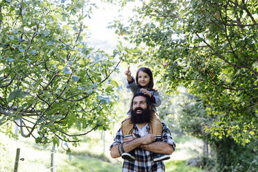 Glücklicher Vater mit Kind auf den Schultern in einem Obstgarten - SODF00334