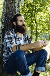 Mann mit Bart sitzt an einem Baumstamm im Wald - SODF00348