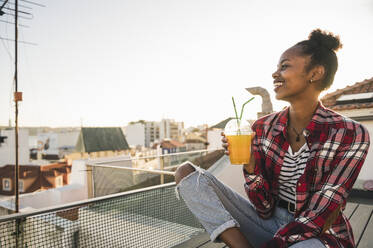Happy young woman having a drink on rooftop at sunset - UUF19453