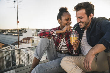 Happy young couple having a drink on rooftop in the evening - UUF19466