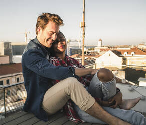 Relaxed affectionate young couple sitting on rooftop in the evening - UUF19478