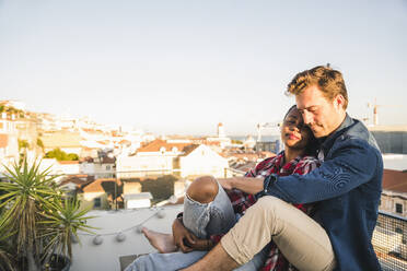 Relaxed affectionate young couple sitting on rooftop in the evening - UUF19479