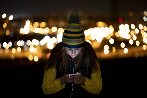 Junge Frau mit Smartphone, die nachts einen Schlapphut trägt - OCMF00880