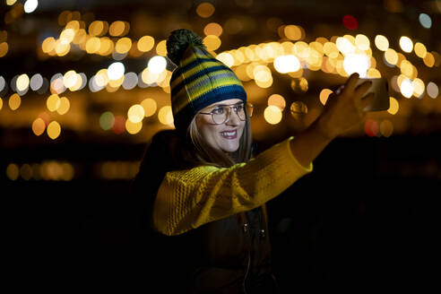 Junge Frau mit Smartphone, die nachts einen Schlapphut trägt - OCMF00881