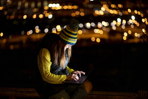 Junge Frau benutzt nachts im Freien einen Laptop - OCMF00882