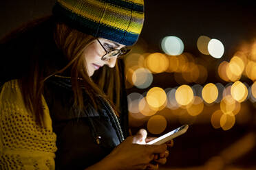 Junge Frau mit Smartphone, nachts mit Hut - OCMF00884