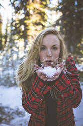Porträt einer Frau, die im Wald stehend Schnee bläst - CAVF68279