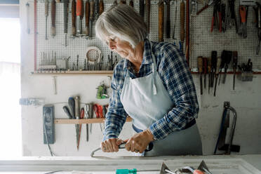 Selbstbewusste Senior-Unternehmerin, die in der Werkstatt eines Geschäfts an einem Fensterrahmen kratzt - MASF14020