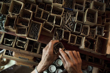 Blick von oben auf eine ältere Verkäuferin, die in einem Baumarkt Nägel aus einem Karton entfernt - MASF14054