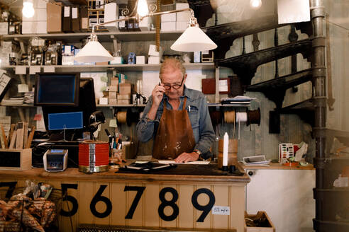Selbstbewusster älterer männlicher Unternehmer bei der Arbeit, während er an der Kasse im Geschäft steht - MASF14065