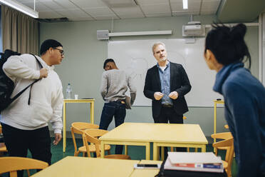 Männlicher Lehrer im Gespräch mit einer Schülerin im Klassenzimmer stehend - MASF14105