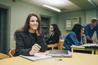 Porträt einer lächelnden Studentin am Schreibtisch im Klassenzimmer - MASF14114