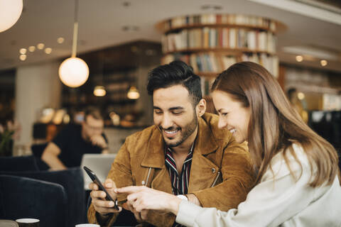Lächelndes Paar, das ein Smartphone benutzt, während es im Restaurant sitzt, lizenzfreies Stockfoto