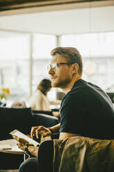 Mid adult man using digital tablet while looking away in restaurant - MASF14139