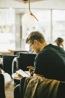 Seitenansicht eines Mannes, der ein digitales Tablet benutzt, während er im Restaurant sitzt - MASF14140