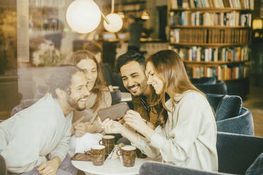 Glückliche Frau zeigt Freunden ihr Smartphone, während sie in einem Restaurant sitzt, gesehen durch Glas - MASF14144