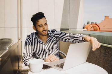 Young man using laptop while sitting in balcony at hotel - MASF14151