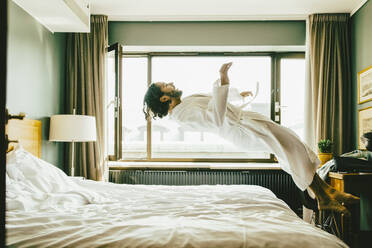 Verspielter Mann im Bademantel springt im Hotel auf das Bett - MASF14161