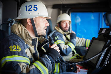 Feuerwehrmann spricht mit Mikrofon, während er mit einem Kollegen im Feuerwehrauto sitzt - MASF14163